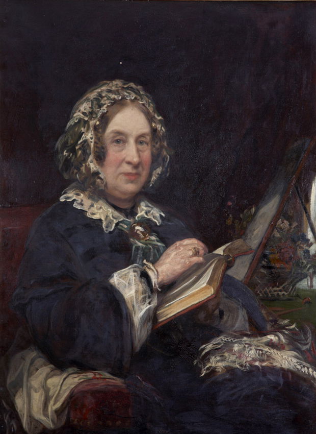 Formal painted portrait depicting a middle-aged woman wearing a dark blue dress with white lace trim and a decorative white lace cap. She is seated in an upholstered chair, holding an open book in her hands, with additional books and papers visible on a nearby table. The subject has a direct gaze toward the viewer and the composition uses rich, dark tones typical of formal portraiture.